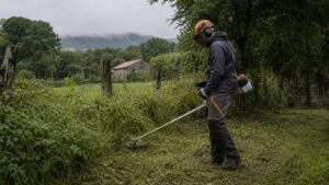 Usuario con desbrozadora trabajando hierba alta en finca humeda