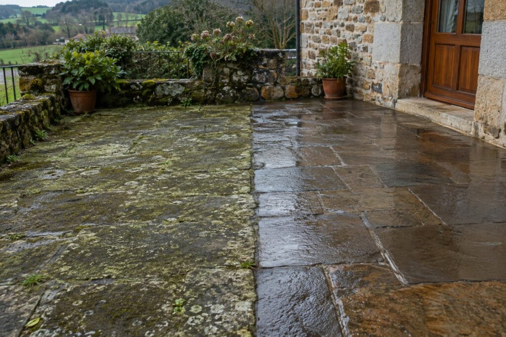 Terraza de losas de piedra a medio limpiar: una mitad con musgo y la otra recién lavada con agua a presión